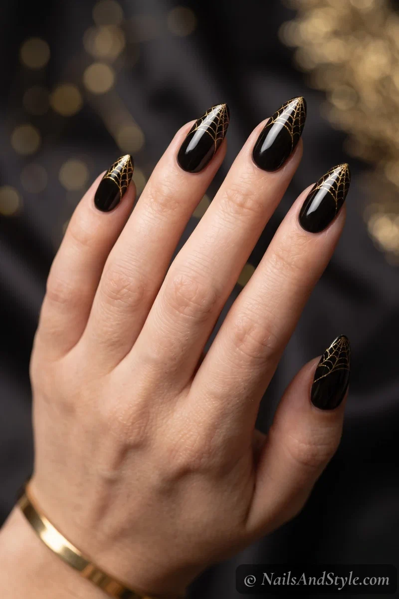 Glossy black almond nails with a delicate gold spider web