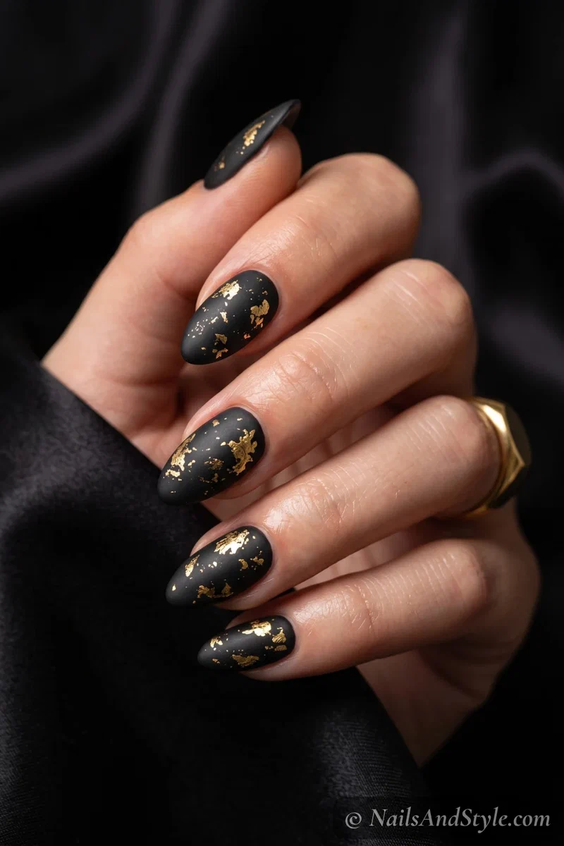 Matte black almond nails with scattered gold foil flakes