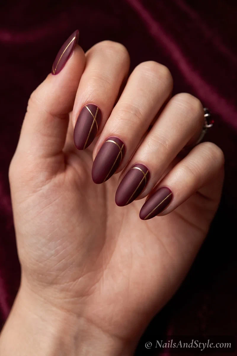 Matte deep burgundy almond nails with thin gold accents