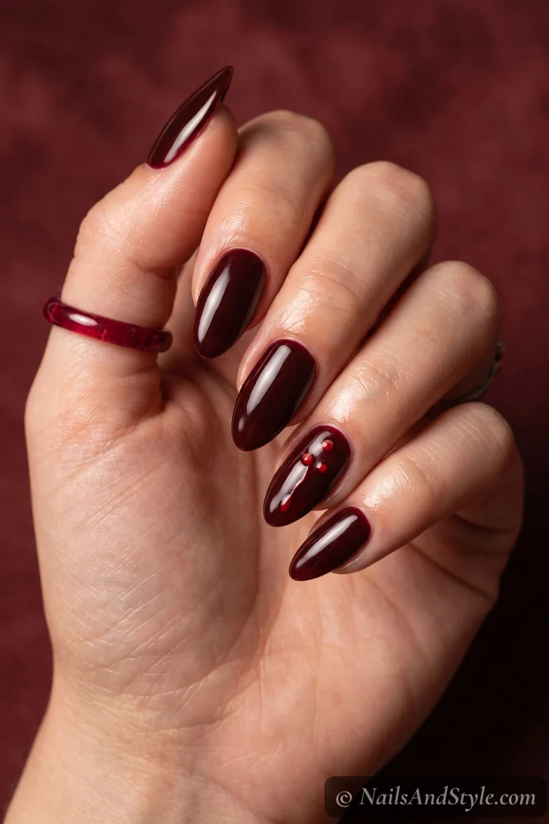 Dark oxblood almond nails with two bite marks and a thin drip