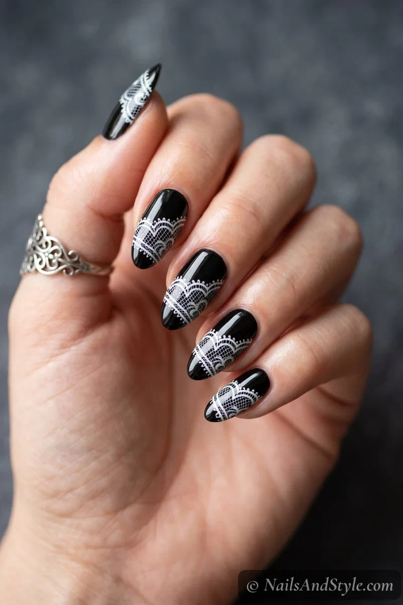 Glossy black almond nails with delicate white lace detailing