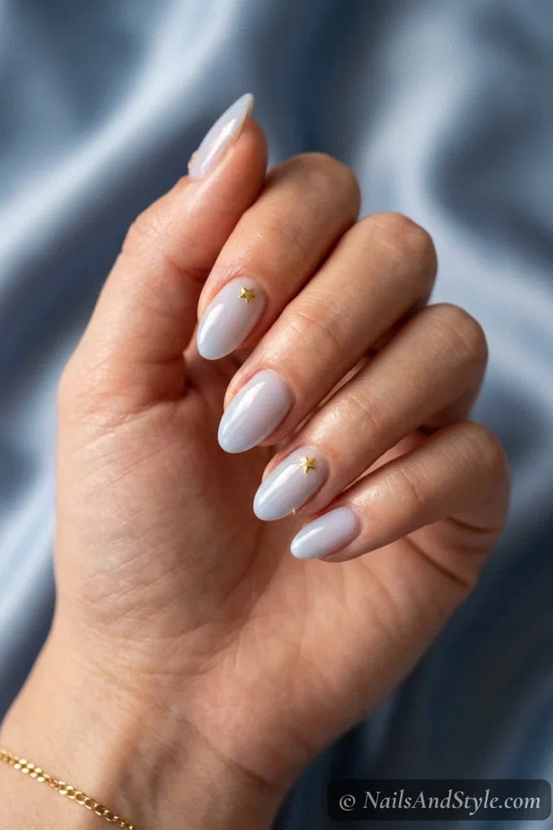 Gold star stud nails with tiny gold star studs near the cuticle over a sheer nude base on short almond nails