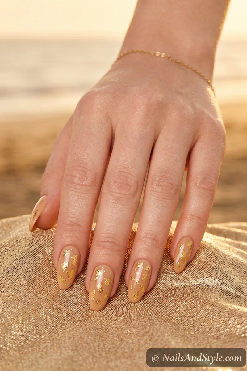 Warm sandy nude nails with gold foil flakes scattered on the surface