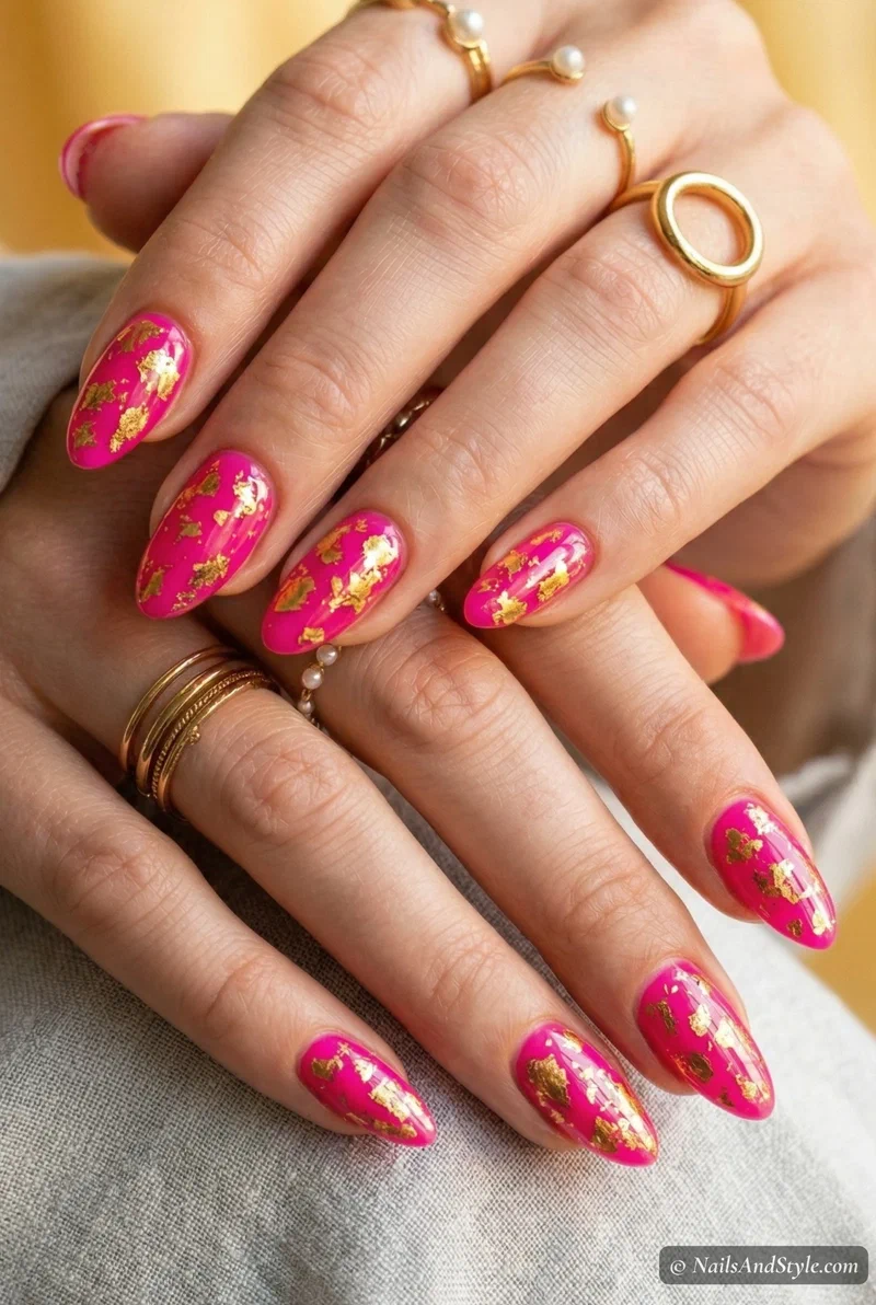 Fuchsia pink nails with gold foil flecks on almond shaped nails