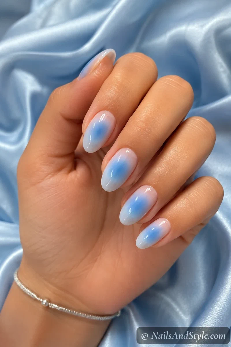 Sky blue aura nails with a soft blue halo blurred over a nude base on medium almond nails