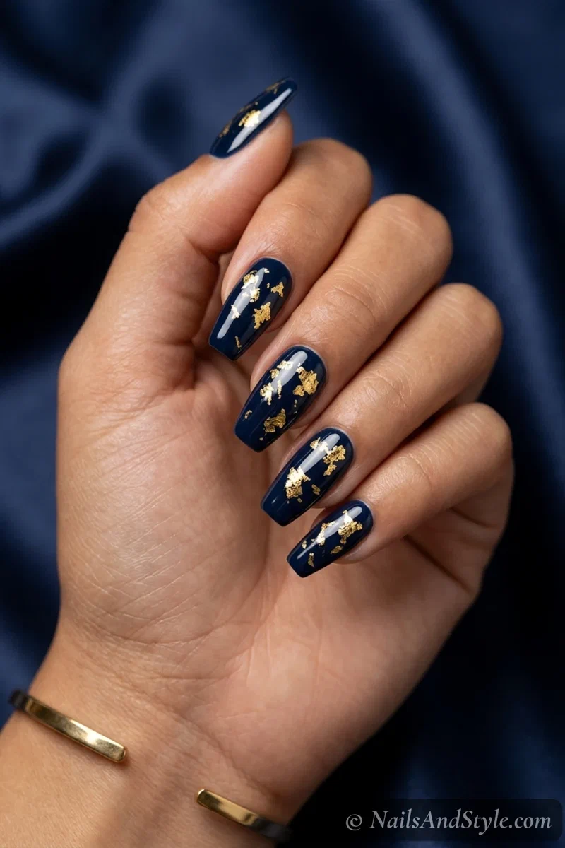 Navy and gold foil nails with scattered gold foil flakes over a deep navy base on medium coffin nails