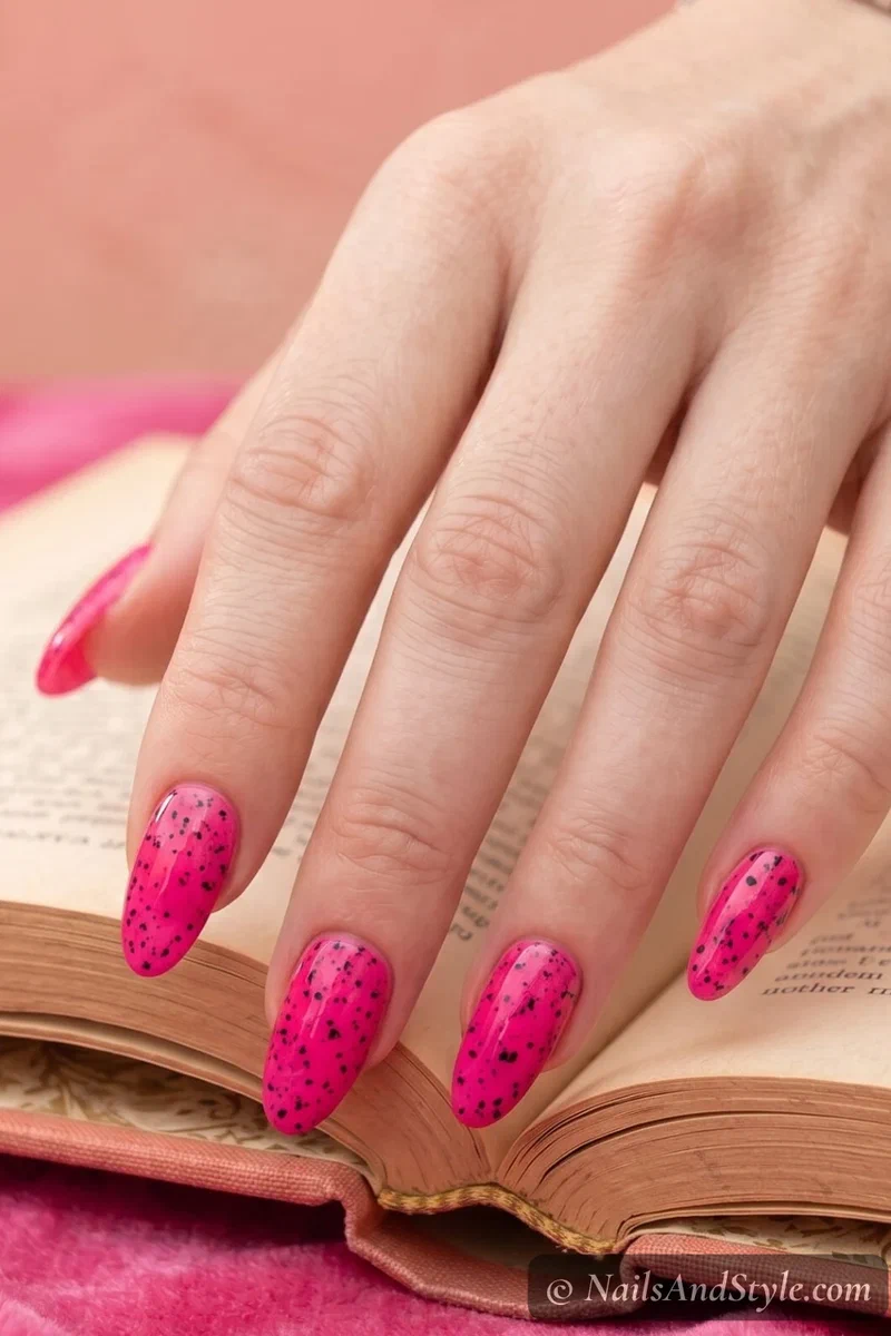 Dragon fruit inspired nails with hot pink base and scattered black speckle dots