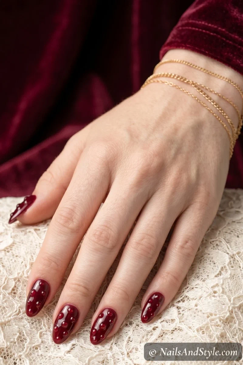 Pomegranate seed nail art with garnet dots on deep wine base and jewel finish