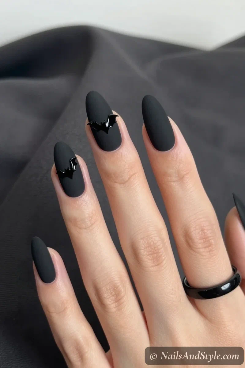 Matte black nails with one glossy black bat detail on an accent nail