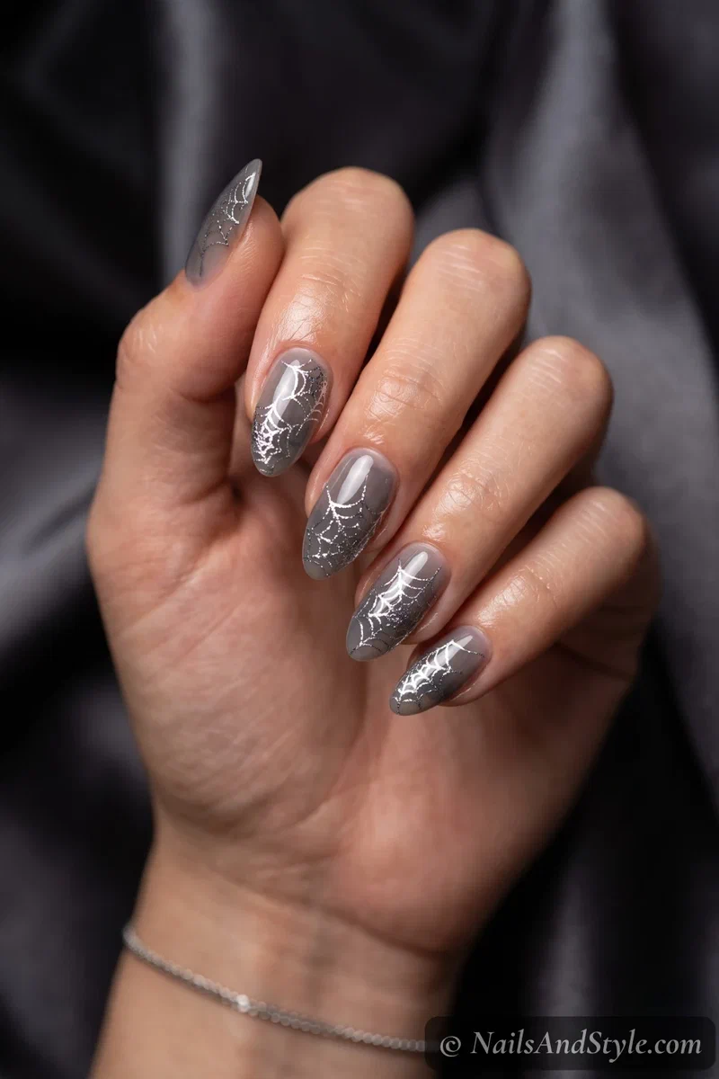 Sheer grey nails with silver foil cobweb decals catching the light