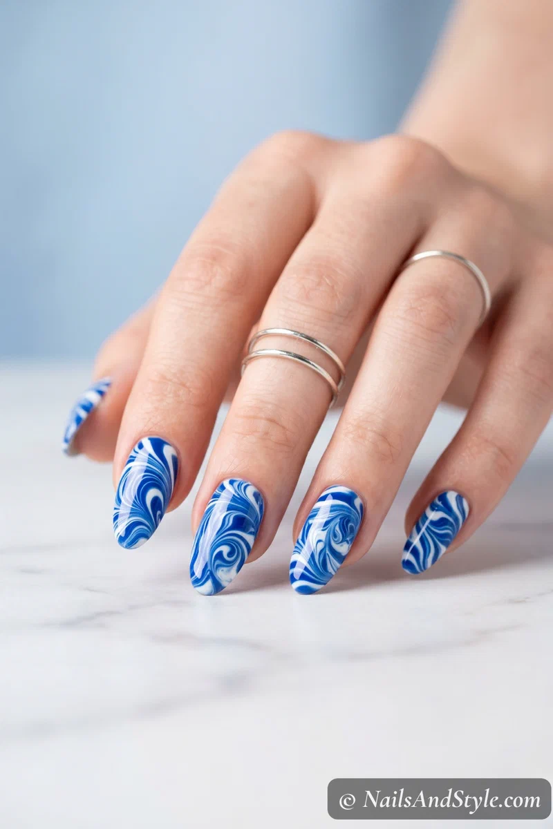 Water marble nails in cobalt blue and white swirl pattern on almond shaped nails