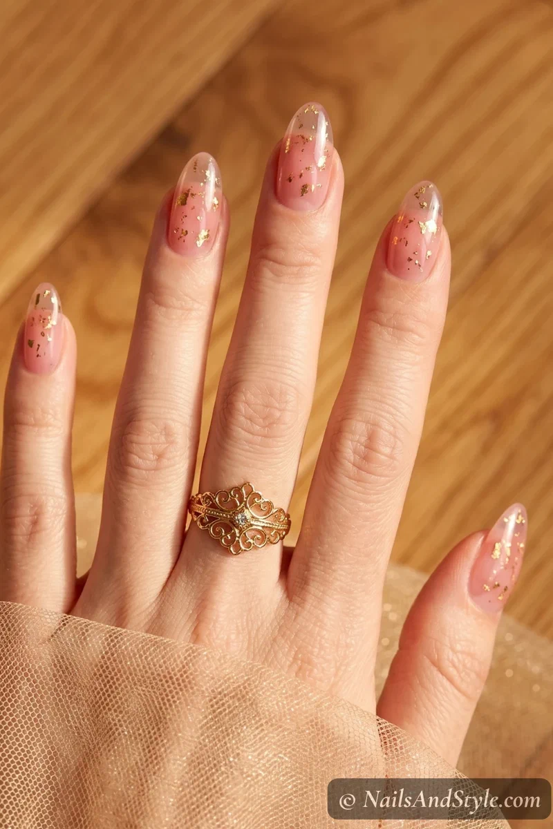 Sheer pink jelly nails with scattered gold foil flakes embedded throughout on medium almond nails