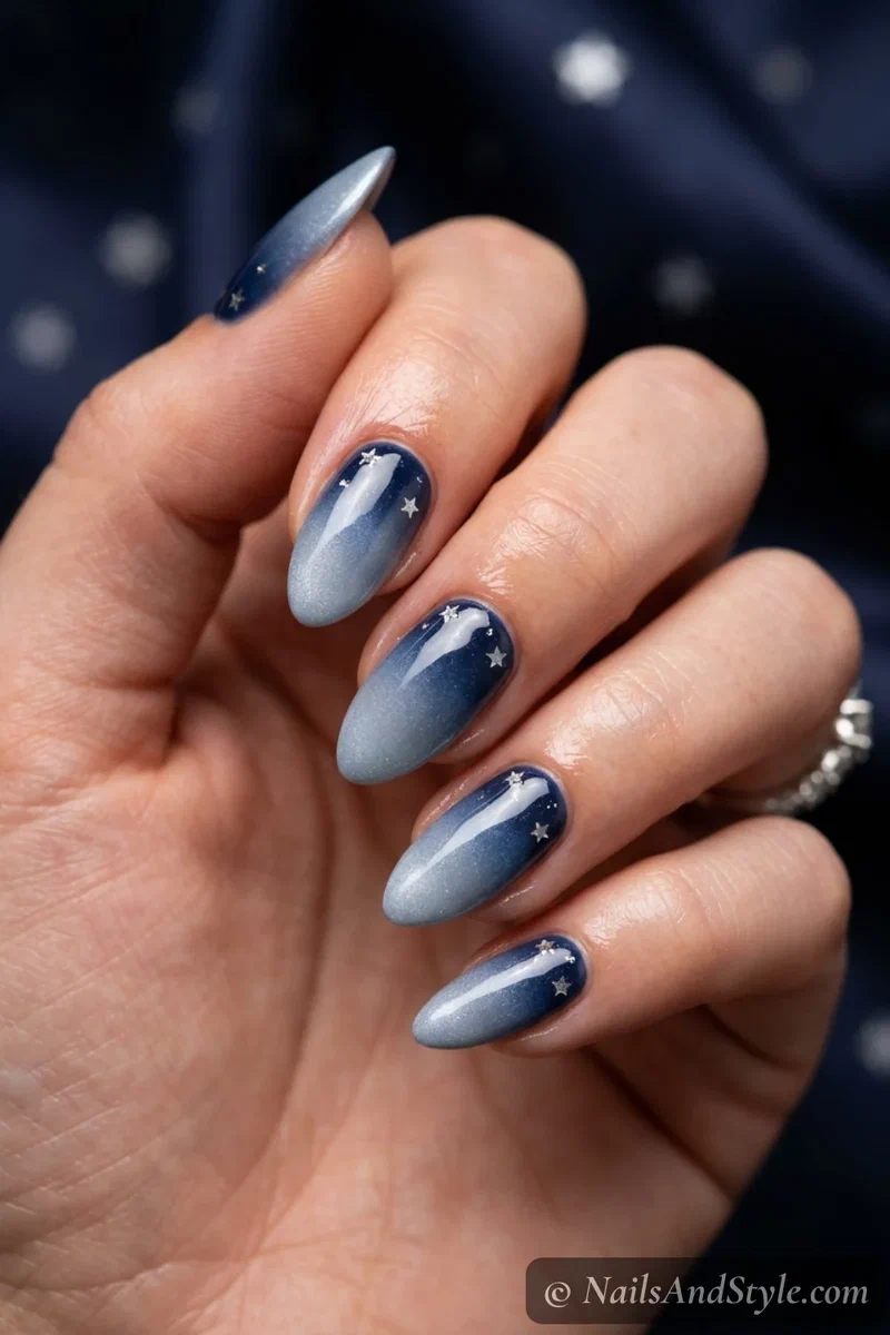 Star studded blue ombre nails fading navy into silver-blue with tiny stars near the cuticle, medium almond nails