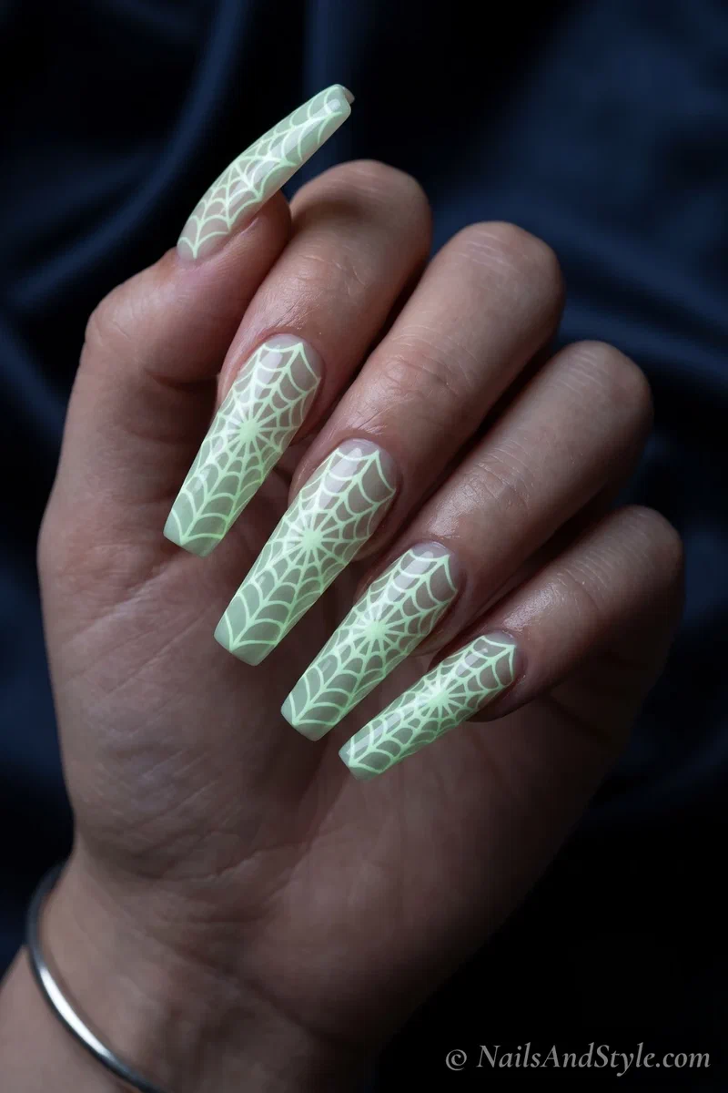 Long black nails with an intricate spider web glowing in the dark