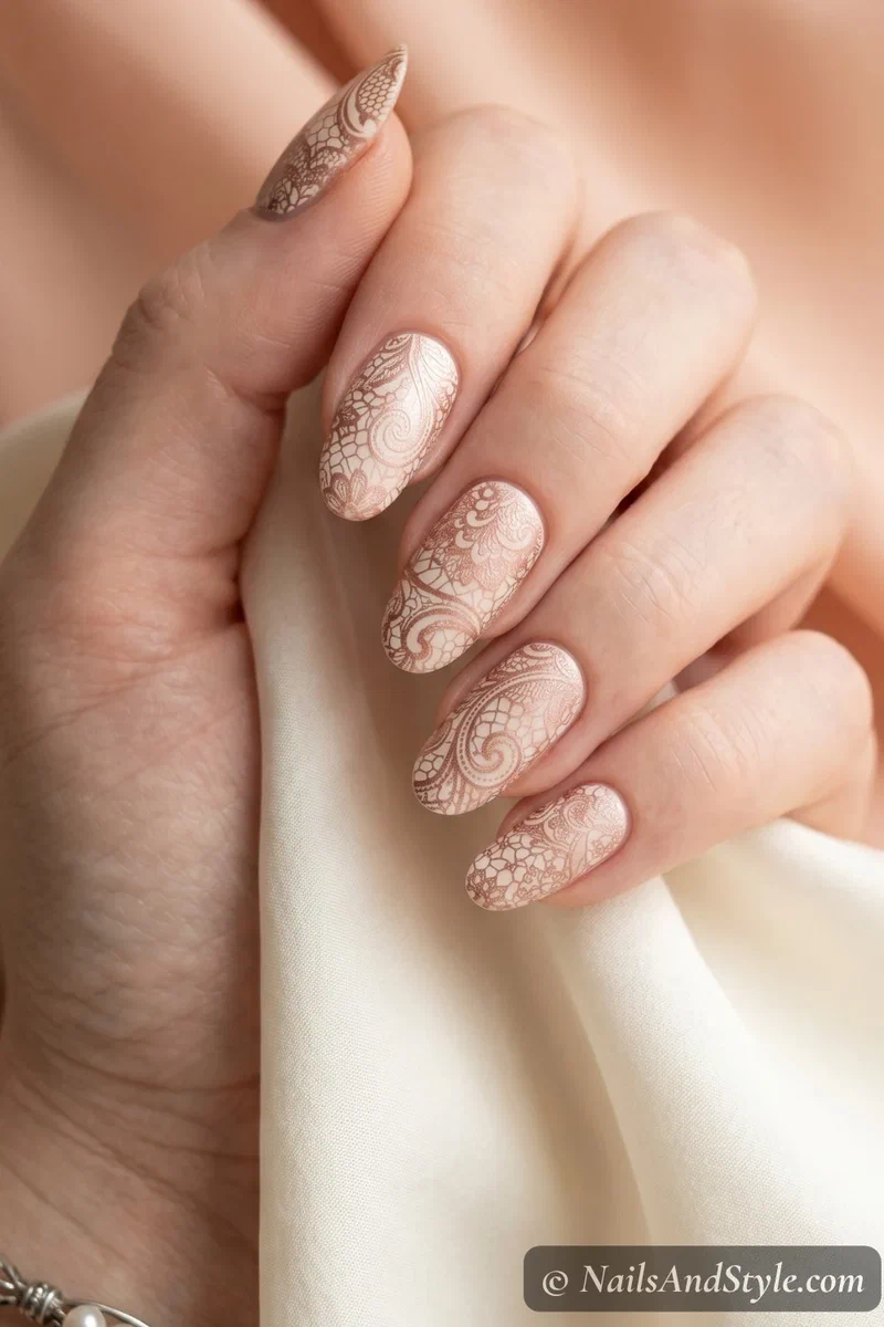 Delicate lace nail stamping in rose gold over a pearl cream base on oval shaped nails