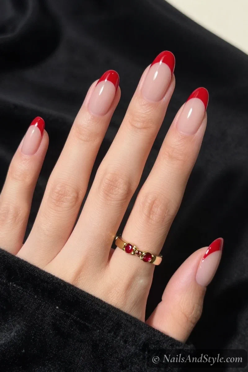 Red French tip nails with clean true-red tips over a sheer nude base on medium almond nails