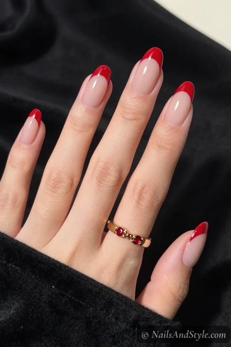 Red French tip nails with clean true-red tips over a sheer nude base on medium almond nails