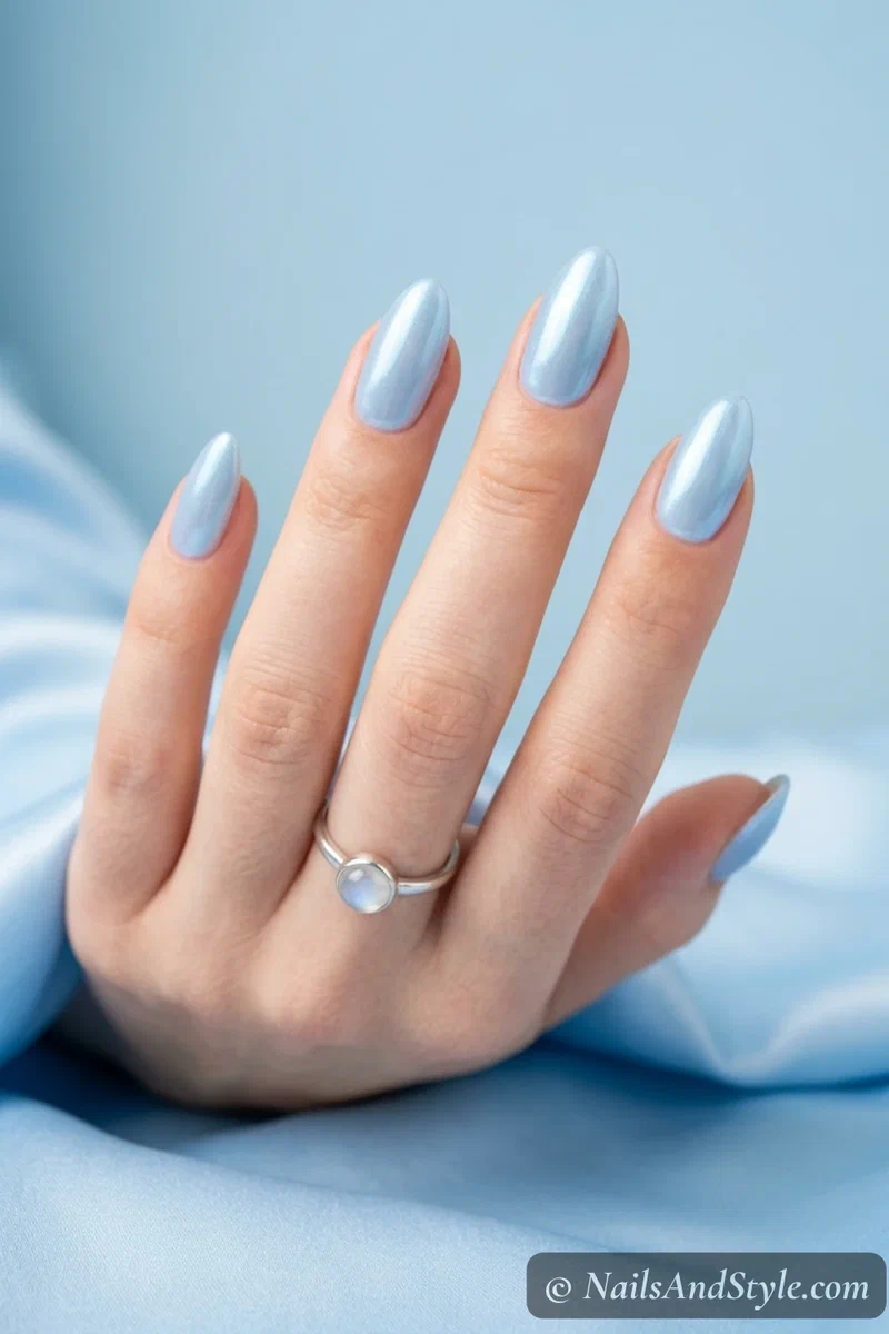Powder blue glazed nails with a pearly luminous chrome sheen over a soft blue base on medium almond nails