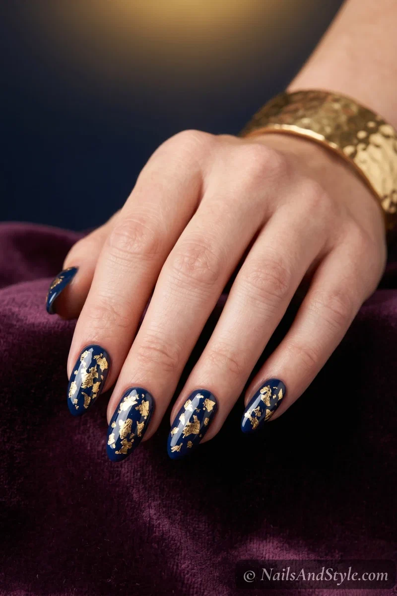 Deep navy nails with scattered pieces of gold foil catching the light