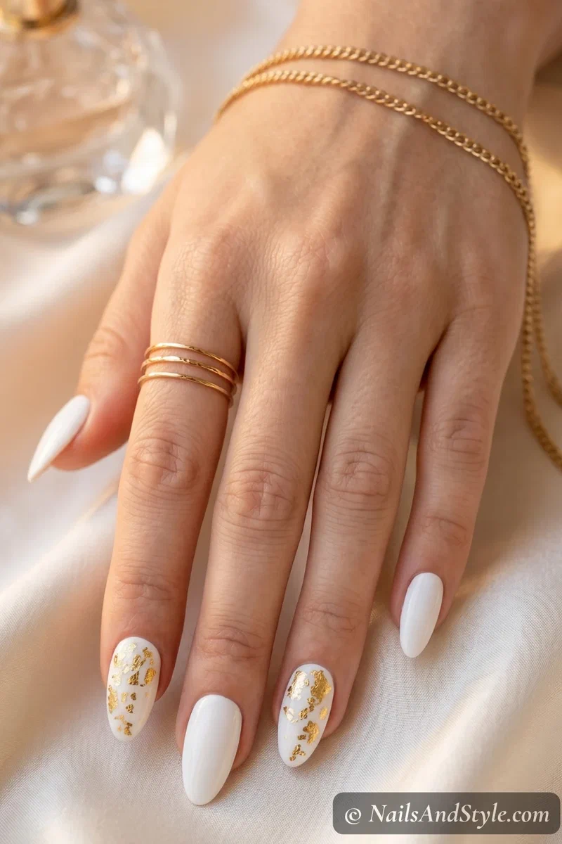 White nails with scattered gold foil accents near cuticle on medium almond nails