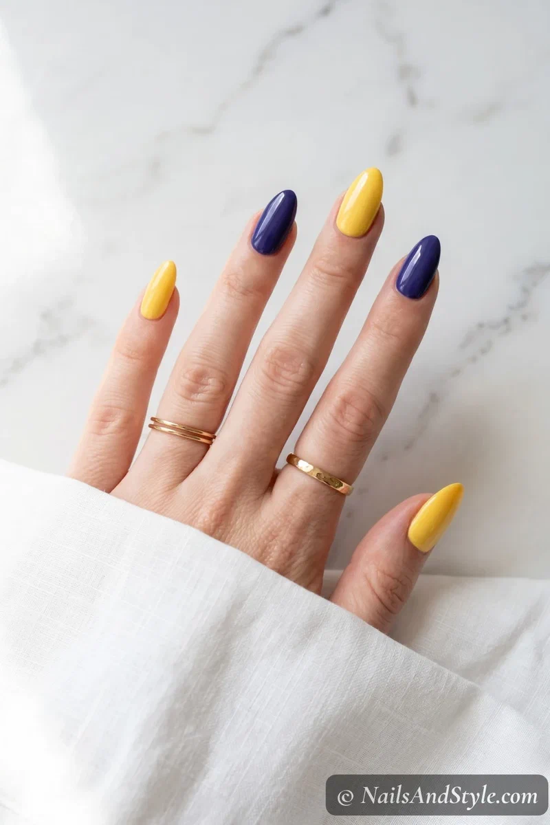 Alternating sunshine yellow and deep blueberry purple nails in solid color block style on short almond nails
