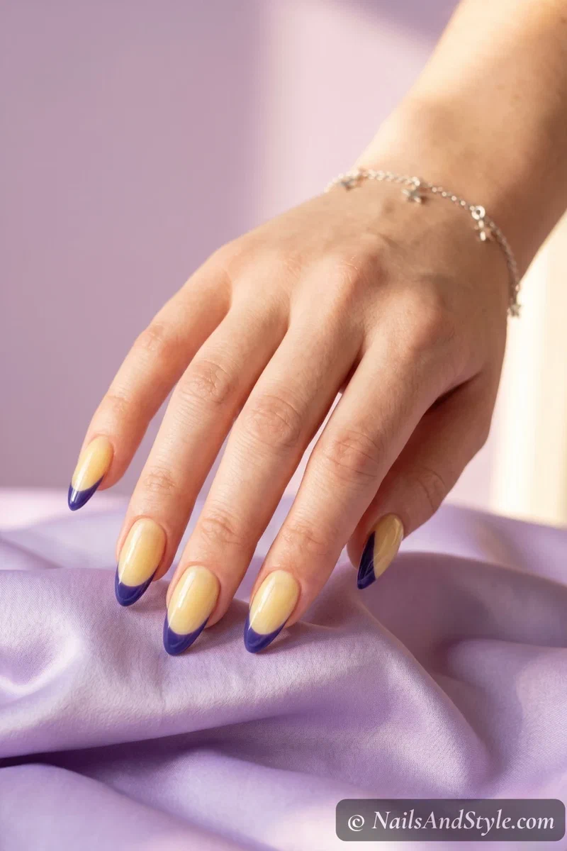 Yellow blueberry French tip nails with butter yellow base and deep purple blueberry tips on medium almond nails